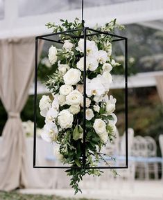 white flowers are hanging from a black metal frame in front of an outdoor dining area