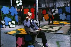 a man sitting on top of a chair in front of an art exhibit with people standing around