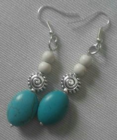 two turquoise and white beads are hanging from silver earwires on a gray surface