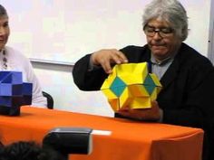 two people are sitting at a table and one is holding an origami cube