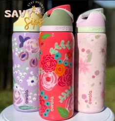 three colorful water bottles sitting on top of a white table in front of a fence