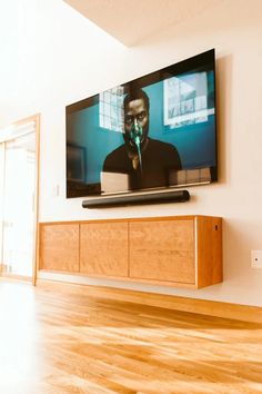 a flat screen tv mounted on the wall above a wooden entertainment unit in a living room