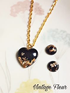 two black heart shaped pendants on a gold plated chain with flowers in the background