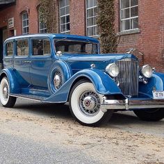 an old blue car parked in front of a brick building