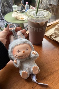 a person holding a small stuffed animal next to a cup of coffee on a table