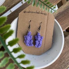 purple crochet earrings sitting on top of a white plate next to a plant