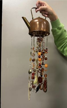 a person is holding a teapot with beads hanging from it's side and there are other items attached to the ceiling