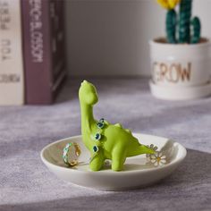 a small green dinosaur figurine sitting in a bowl on a table next to a cactus