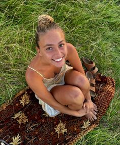 a young woman sitting on top of a rug in the grass with her legs crossed