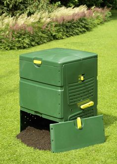 two large green boxes sitting on top of a grass covered field next to bushes and flowers