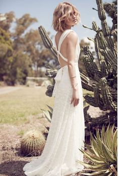 a woman standing in front of a cactus wearing a white dress with an open back