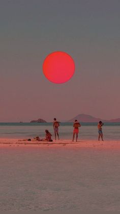 three people standing on the beach under a red ball