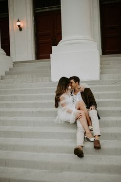 a man and woman are sitting on the steps kissing in front of a white building