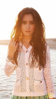 a woman standing in front of the ocean with her hand on her hip and wearing a white jacket