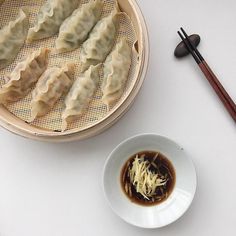 a plate of dumplings with sauce and chopsticks next to it on a white table