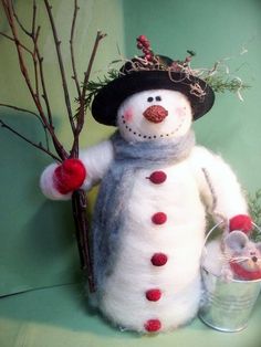 a snowman with a hat and scarf holding a branch in his hand while standing next to a bucket filled with berries