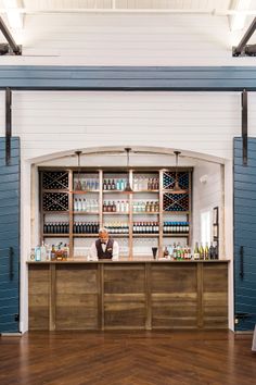 a man behind the bar at a wine tasting event in a building with blue shutters