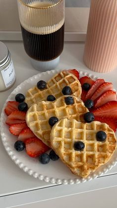 two waffles with strawberries and blueberries on a plate next to a cup of coffee