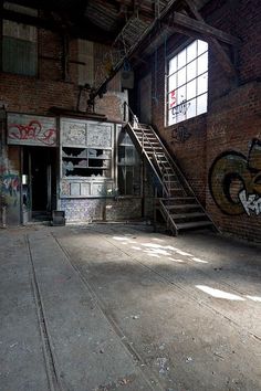 an empty room with graffiti on the walls and stairs leading up to a second floor