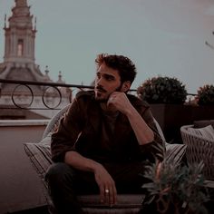 a man sitting on top of a chair next to a potted plant with a clock tower in the background