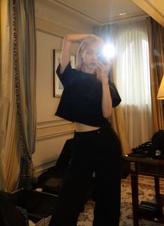 a woman taking a selfie in front of a mirror wearing black pants and crop top