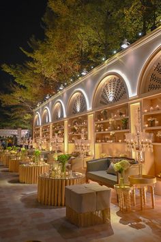 an outdoor seating area at night with lights on the ceiling and tables in front of it