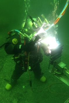 a man in scuba gear is working on an underwater device with green light coming from it