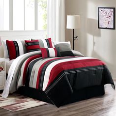 a bed with red, black and white comforters in a room next to a window