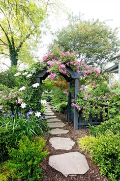 a garden with lots of flowers and plants around it, along with a stone path