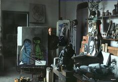 a man standing next to some paintings in a room with other items on the floor