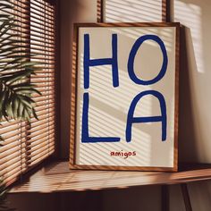 a sign that says hola on it next to a window with blinds and a potted plant