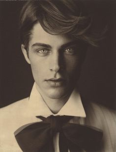 a black and white photo of a young man with a bow tie around his neck