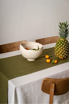 a table topped with a bowl of fruit next to a pineapple and oranges