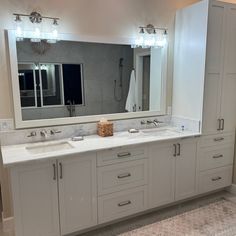 a large bathroom with two sinks and mirrors on the wall, along with white cabinets