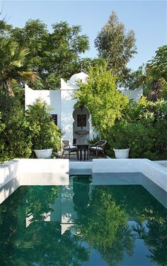 the pool is surrounded by greenery and white walls, with an outdoor dining area in the background