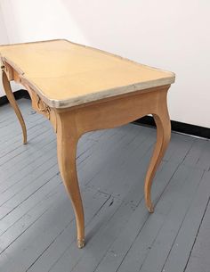 an old wooden table sitting on top of a hard wood floor next to a white wall