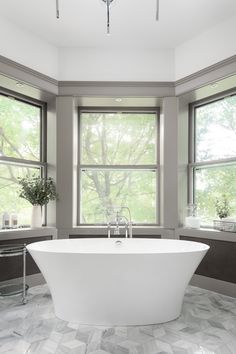 a large white bath tub sitting in a bathroom next to two windows and a sink