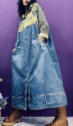 a woman standing in front of a purple wall wearing a denim dress and brown boots