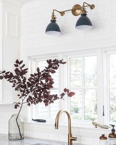 a white kitchen with marble counter tops and brass faucet lighting over the sink