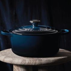 a blue casserole sitting on top of a wooden table next to a black curtain