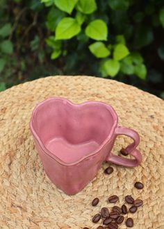 a pink heart shaped mug sitting on top of a straw hat next to coffee beans