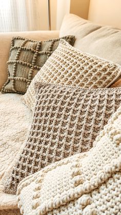 two crocheted pillows sitting on top of a white couch next to a window