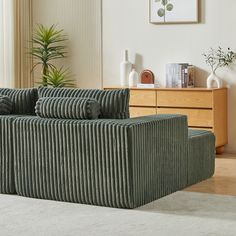 a living room scene with focus on the couch and chair in the foreground, there is a potted plant next to it