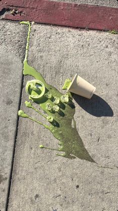 a piece of green paint on the ground next to a roll of paper and a cup