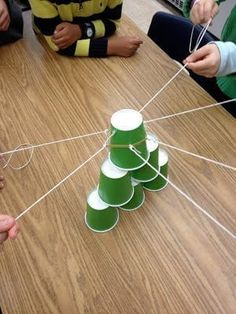 children are sitting at a table playing with paper cups and stringing around the tree