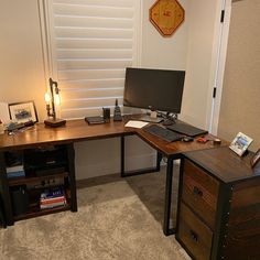 a desk with a computer monitor and keyboard on top of it next to a window