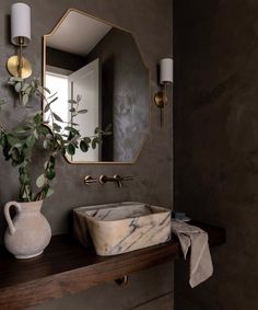 a bathroom sink sitting under a mirror next to a vase with a plant in it