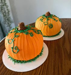 two pumpkin shaped cakes sitting on top of white plates with green leaves and swirls