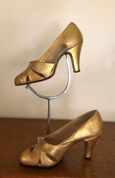 a pair of gold high heeled shoes sitting on top of a wooden table next to a lamp