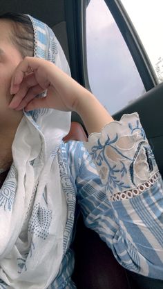 a woman sitting in the back seat of a car wearing a blue and white scarf